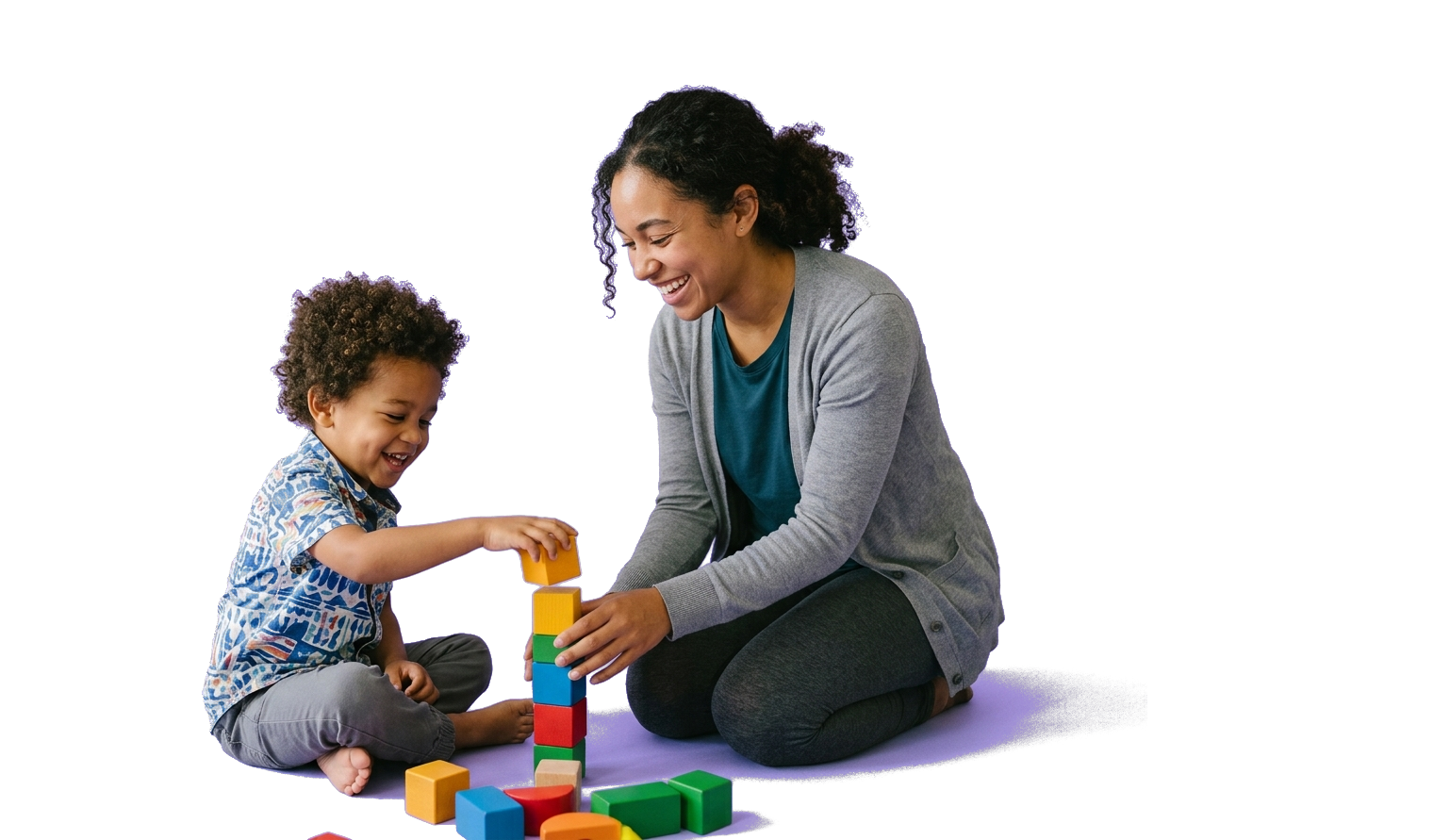 A behavior technician sitting on the floor stacking colorful blocks with a smiling young child during a play-based session.